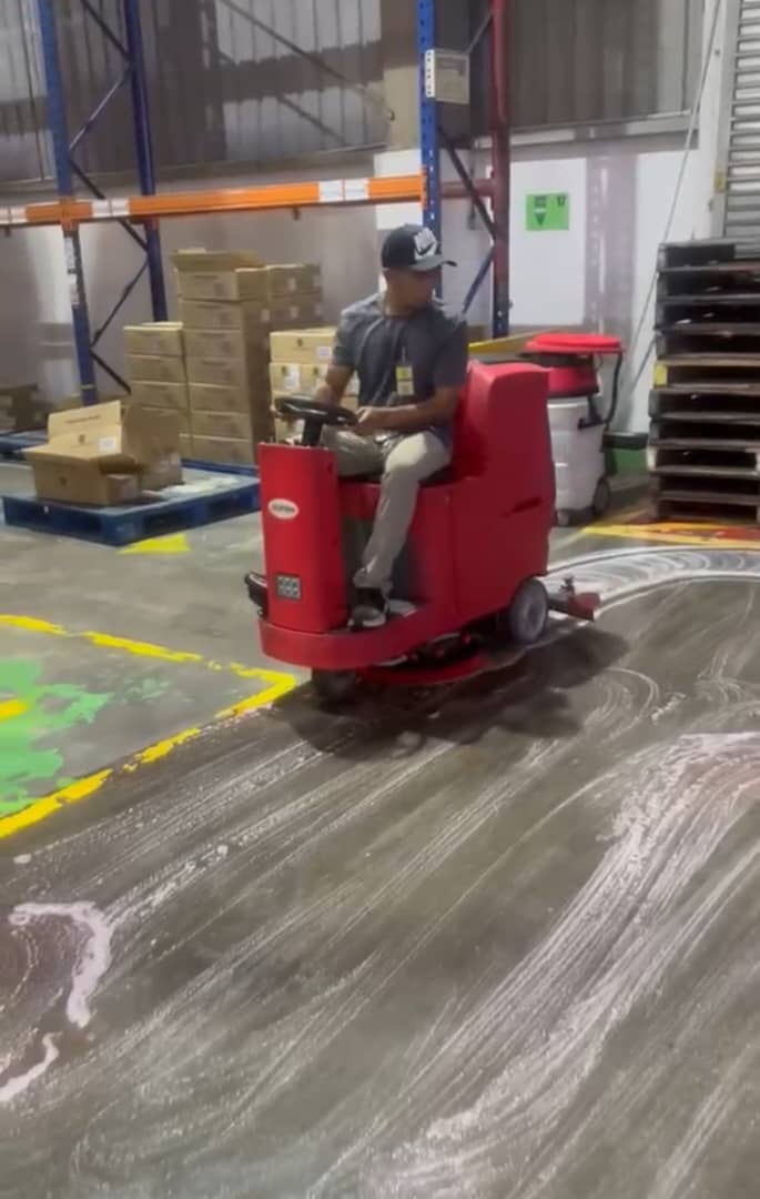 Ride-on auto-scrubber cleaning a warehouse floor